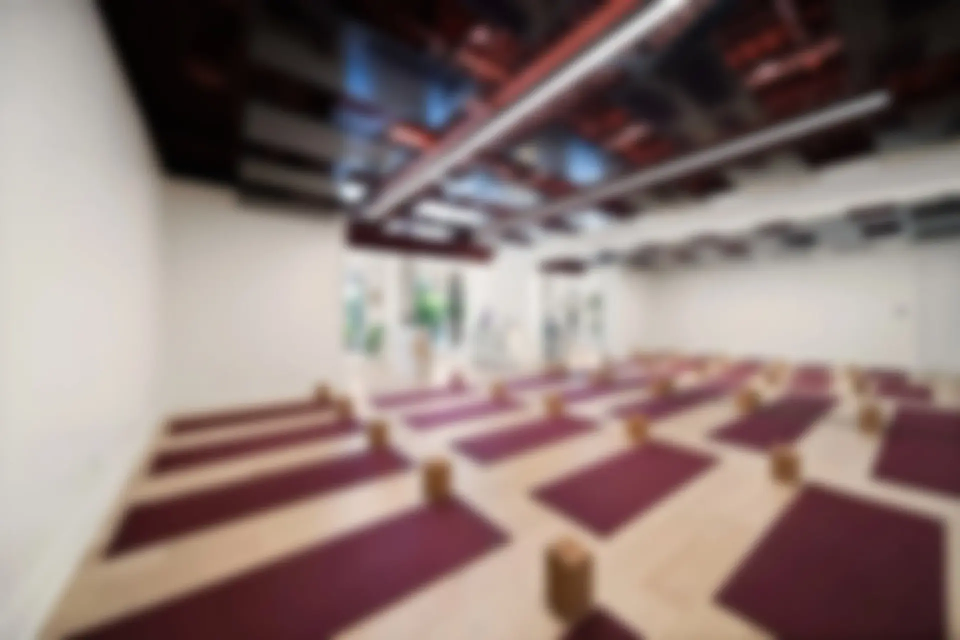 A softly blurred view of the Sora studio with rows of burgundy mats and cork blocks under the ceiling