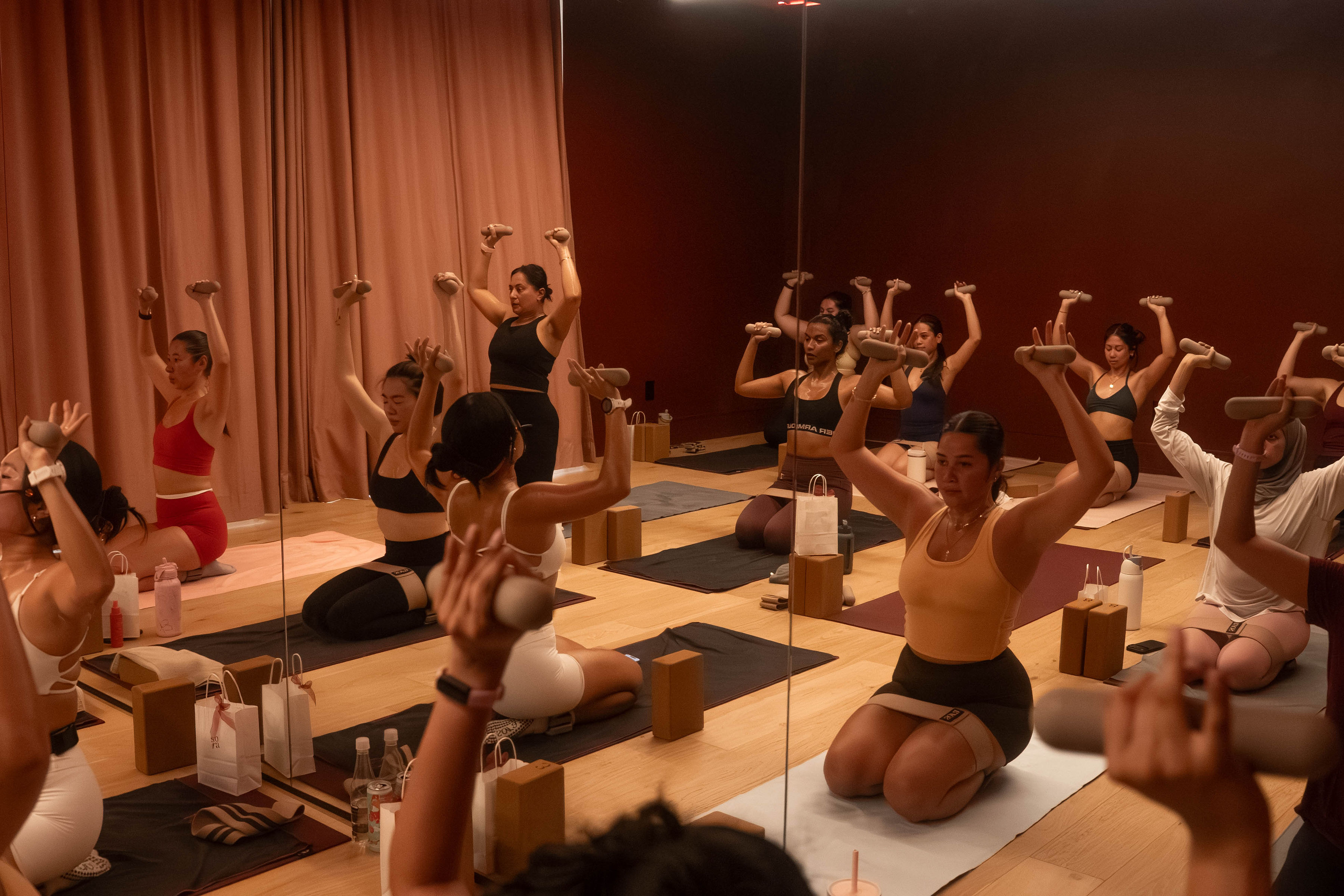 Women in a heated mat Pilates class at Sora Studio, including a participant in a hijab and long sleeves, lifting hand weights